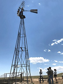 group of people gathered by a windmil in arid field